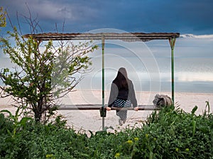 Rear view of a woman sitting on a bench in front of the sea.