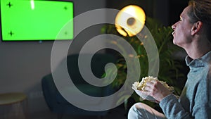 Rear view of a woman sitting on a sofa in the living room in the evening and watching a green TV screen mockup, is