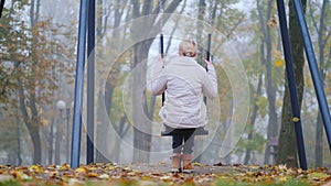 Rear view of a woman sitting on a swing in a park where there is heavy fog. Loneliness concept