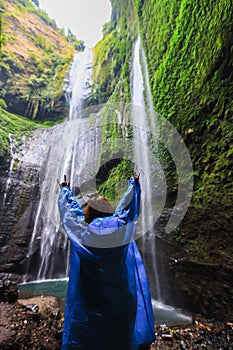 Rear view of woman standing in front of waterfall and hands outstretched. Winner near waterfall. Sport and active life concept. Tr