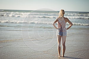 Rear view of woman standing with hands on hip at beach