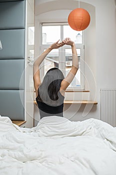 Rear view of woman stretching in bed after wake up in morning