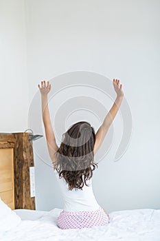 Rear view of young woman stretching in bed after wake up in morning with sunlight