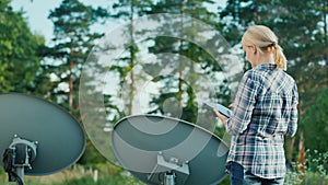 Rear view of Woman tunes satellite dishes outdoors, uses tablet