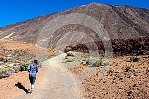 Rear view on woman walking on panoramic hiking trail leading to Pico del Teide in volcano Mount Teide National Park, Tenerife photo
