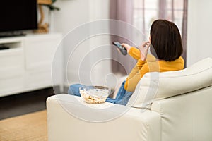 Rear view of woman watching TV with popcorn at home
