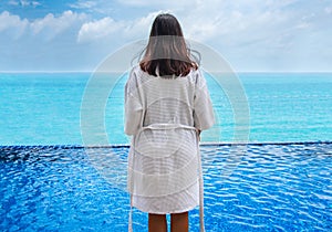Rear view of woman wearing bathrobe and looking into the pool with sea in background