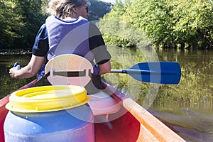 Rear view of a woman wearing a life jacket paddling a canoe down a river in europe