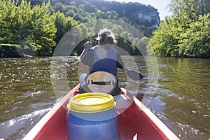 Rear view of a woman wearing a life jacket paddling a canoe down a river in europe