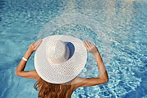 Rear view of woman in white hat sitting near pool on a sunny day. Sea travel concept with place for your text