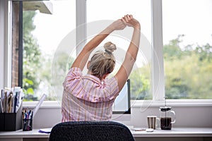 Rear View Of Woman Working From Home On Computer  In Home Office Stretching At Desk