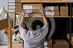 Rear view of young African American female manager of warehouse taking box