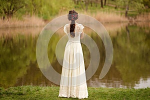 Rear view of a young anonymous bride in a beautiful full wedding dress, with hairstyle, looking down, nature background.