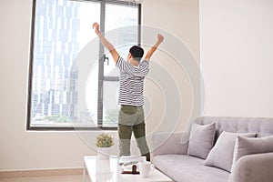 Rear view of a young Asia man stretching his arms near window at