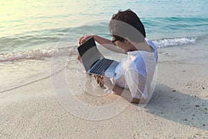 Rear view of young Asian man with laptop lying down on the sandy of beach.