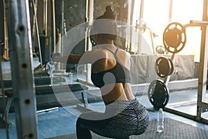 Rear view of young asian woman in sportswear doing squat at health club