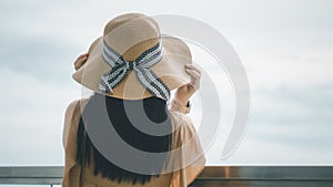 Rear view young Asian woman standing of happy attractive with hands holding sun hat up, sunny day, summer sea, blue sky background