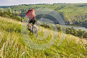 Rear view of the young attractive cyclist riding mountain bike in the summer meadow.