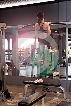 Rear view of a Young attractive woman pulling up on a Chin up bar exercise in a Gym.