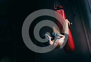 Rear view of young beautiful sportswoman working at her abdominal muscules on a red punching bag on dark background. Sport,