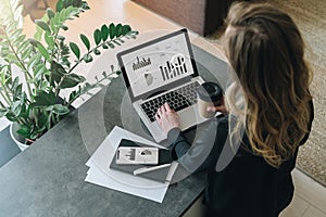 Rear view.Young businesswoman is standing near table,working on laptop with graphs, charts,diagrams, schedules on screen