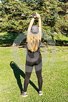 Rear view of a young Caucasian woman in sportswear with arms outstretched in a park. Concept of outdoor pursuit in springtime and