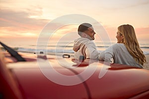 Rear View Of Young Couple Chatting By Car At Beach Watching Sunrise Together photo