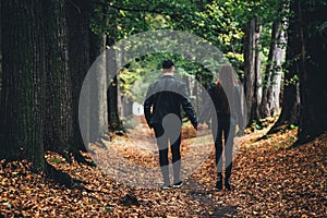 Rear view of young couple in love walking in the autumn park holding hands.