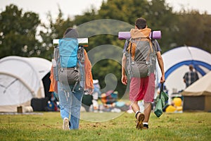 Rear View Of Young Couple Meeting At Summer Music Festival With Camping Equipment