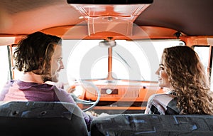 A rear view of young couple on a roadtrip through countryside, driving minivan.