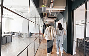 Rear view of young couple walking to office along walkway in open plan building