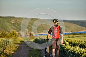 Rear view of the young cyclist riding bicycle on the road of the field.