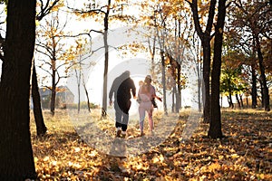 Rear view of young family with one small children walking in autumn nature. Walk in the autumn park.