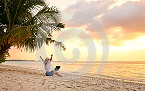 Rear view of young female freelancer in straw hat celebrating success. while working remotely on the tropical sandy beach at