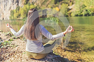 Rear view of young female practicing yoga at mountain lake. Healthy lifestyle and nature concepts