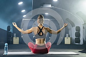 Rear view of young fit woman in sportswear doing yoga at gym