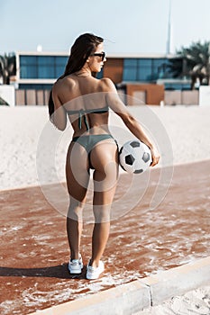 Rear view of young fit woman wear sunglasses in green bikini with football ball play on the beach