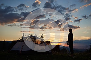 Rear view of young lady standing on top of mountain near camping at sunrise enjoying the view