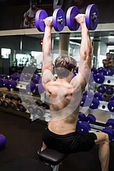 Rear view of a young male doing heavy weight exercise with dumbbells.