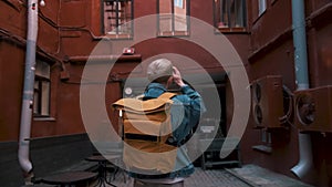 Rear view of a young male traveller walking around the city with yellow backpack and taking photos.