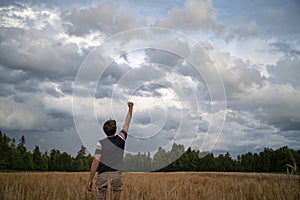 Rear view of a young man standing victorious in the middle of beautiful golden wheat field