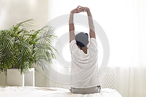 Rear View Of Young Man Stretching Arms In Bed After Waking Up