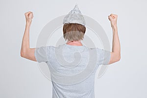 Rear view of young man with tinfoil hat as conspiracy theory concept raising fists