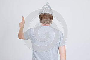 Rear view of young man with tinfoil hat as conspiracy theory concept touching something