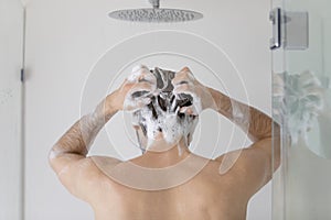 Rear view young man washing hair, standing in bathroom