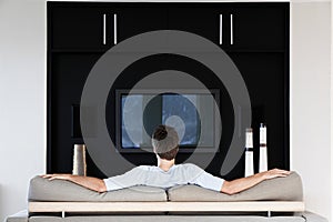 Rear view of young man watching television while sitting on couch in living room