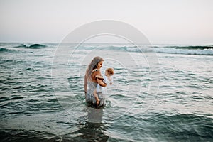 Rear view of young mother with a toddler girl walking in sea on summer holiday.