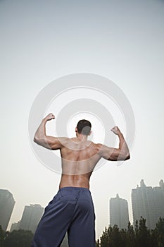 Rear view of young, muscular man with no shirt on flexing his back muscles, outdoors in Beijing, China