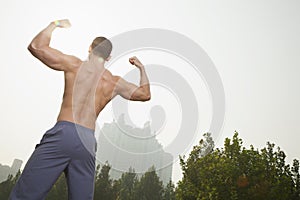 Rear view of young, muscular man with no shirt on flexing his back muscles, outdoors in Beijing, China, with a camera tilt