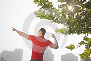 Rear view of young muscular man stretching by a tree, arms raised and fingers pointing towards the sky in Beijing, China with lens